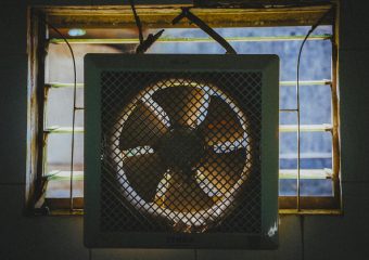 A vintage exhaust fan installed in a rustic window frame, casting dramatic shadows.