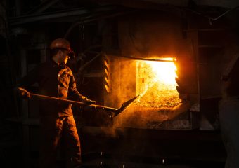 Blue-collar worker managing furnace in an industrial plant setting.